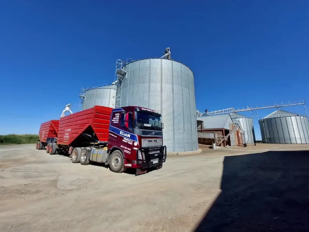 Edan Vehicle & Asset Hire truck with red interlink bottom dumper trailers parked at a grain storage facility in South Africa.