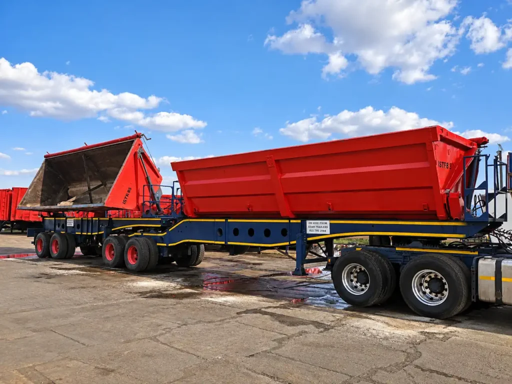 Red interlink side tipper trailer with its bin raised, available for hire from Edan Vehicle and Asset Hire.