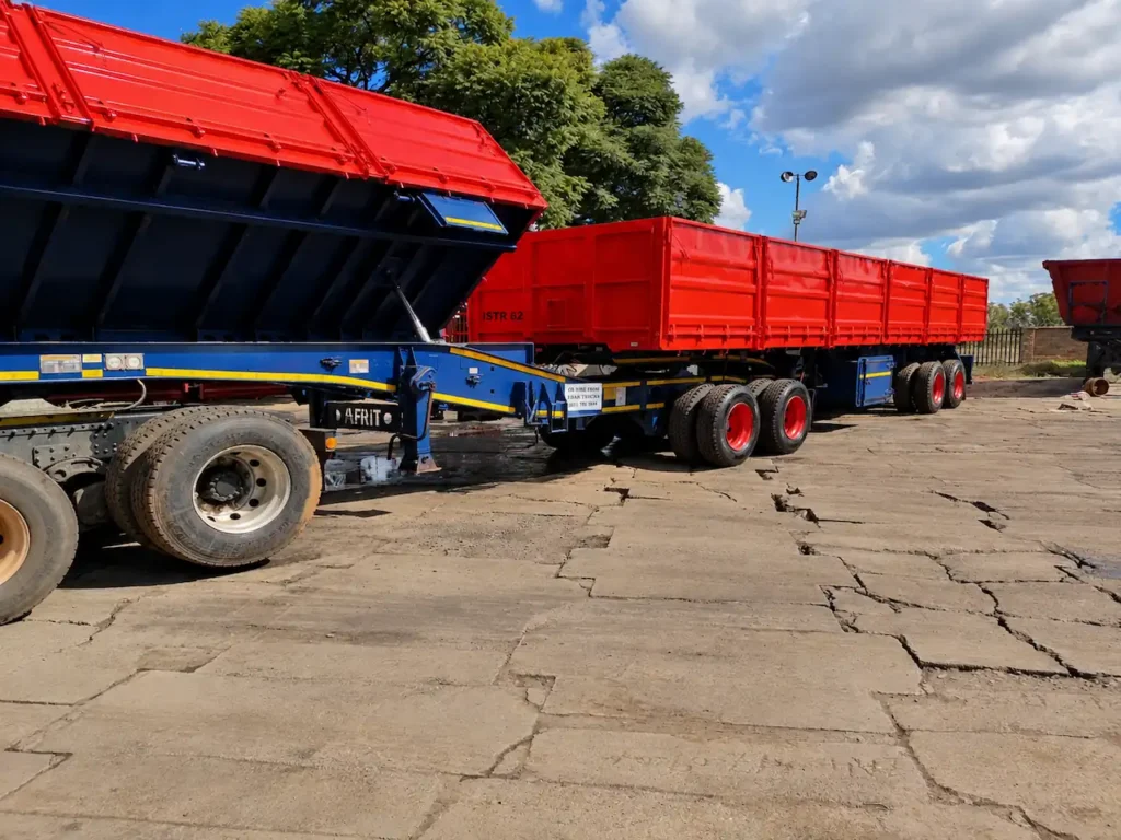 Raised red dropside tipper body showing the blue trailer chassis, hydraulic lifting mechanism and wheels.