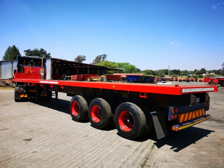 Rear view of a tri-axle flat deck truck trailer for hire from Edan Vehicle & Asset Hire in South Africa, for heavy-duty freight, machinery and general cargo transport.
